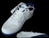 A white and navy blue athletic shoe resting inside an open shoebox with tissue paper, set against a background of cardboard boxes and shelving.