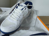 A white and navy blue athletic shoe resting inside an open shoebox with tissue paper, set against a background of cardboard boxes and shelving.