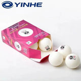 Three white table tennis balls with black YINHE logos spill out of a pink product box on a clean white background, with the YINHE brand logo displayed in the top left corner.